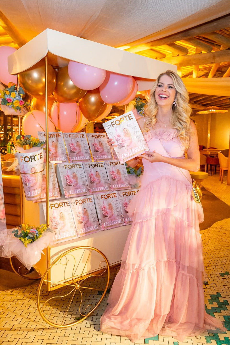 Karina Bacchi segurando a Revista Forte ao lado de um carrinho com várias revistas